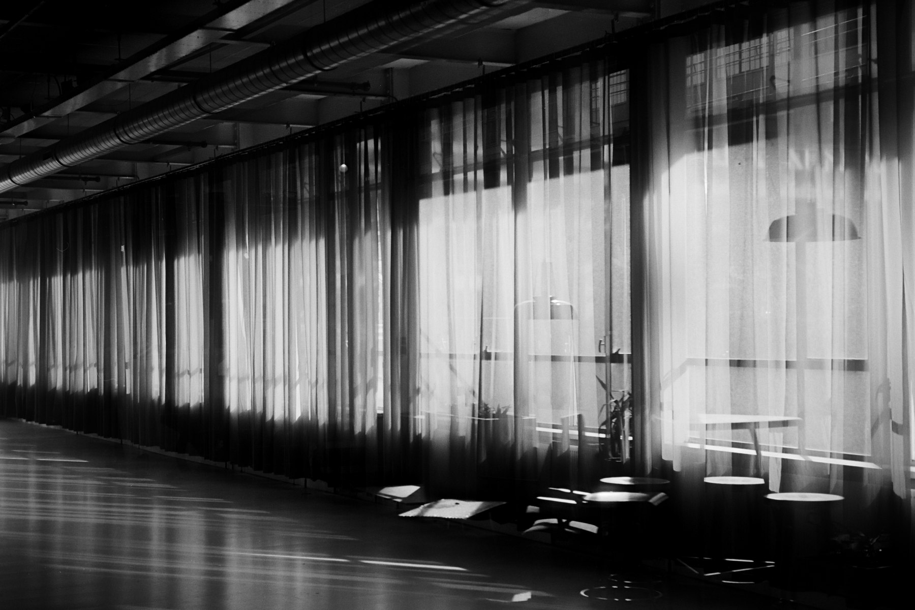 Black-and-white photograph by Rik in which light through curtains shapes an interior.