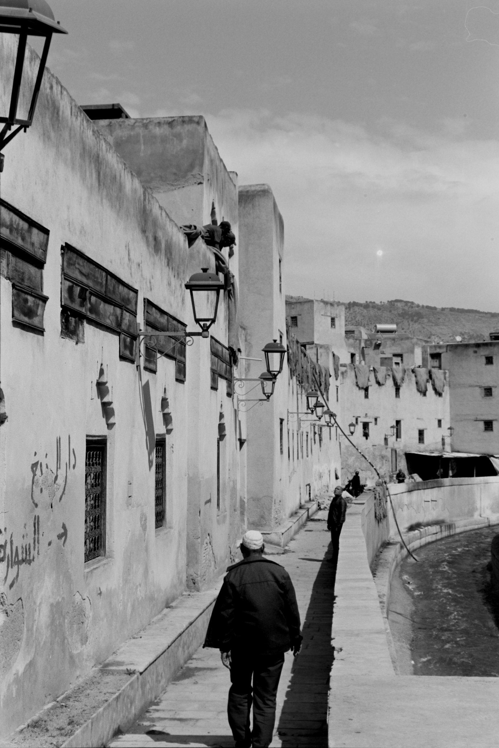 Black-and-white street photograph by Rik showing a pedestrian in a narrow street.