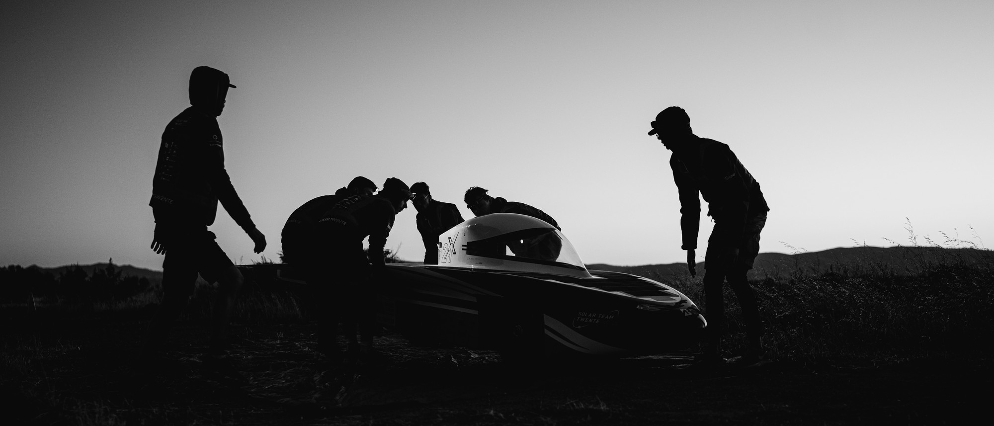 Black-and-white documentary photograph of people around a sports car, photographed by Cas van Laar.