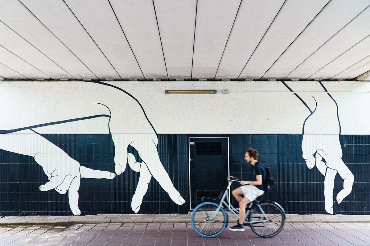 Cyclist passing the Walking Hands mural at Neckerspoel in Eindhoven, with large white hands on a dark wall.