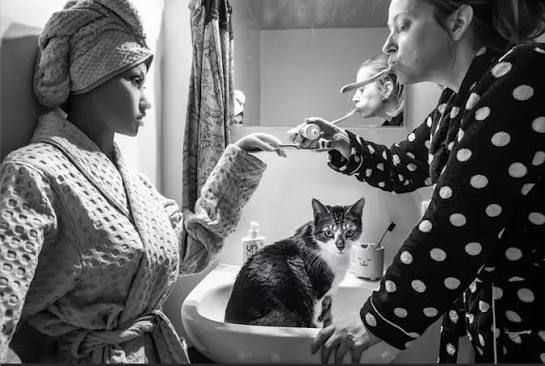 Hanneke Wetzer and the doll Nadiah in a staged bathroom scene from Living Alone (Together), with a cat in the foreground.