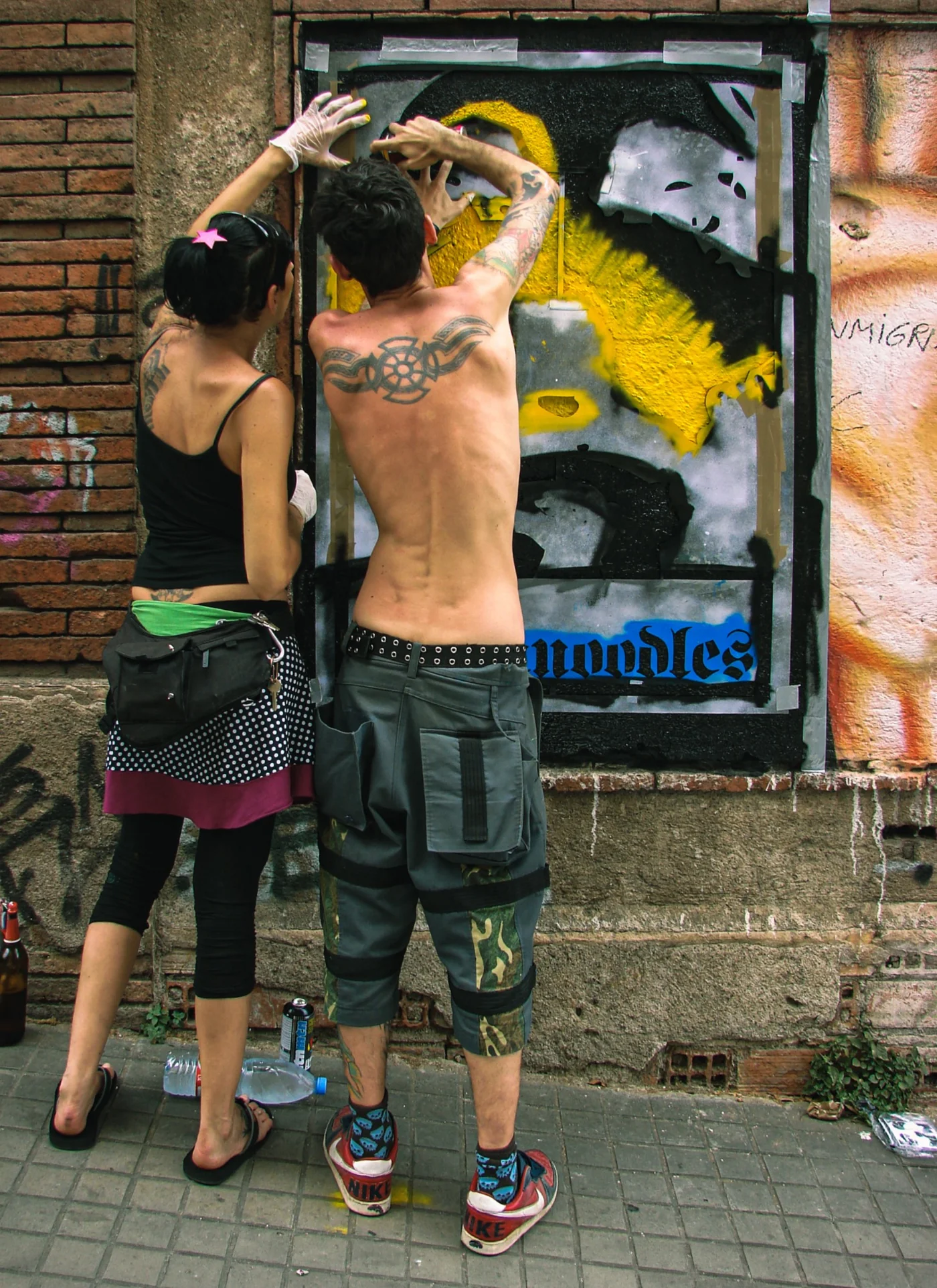 Twee makers werken samen aan een stencil- en street-artwerk op een muur.