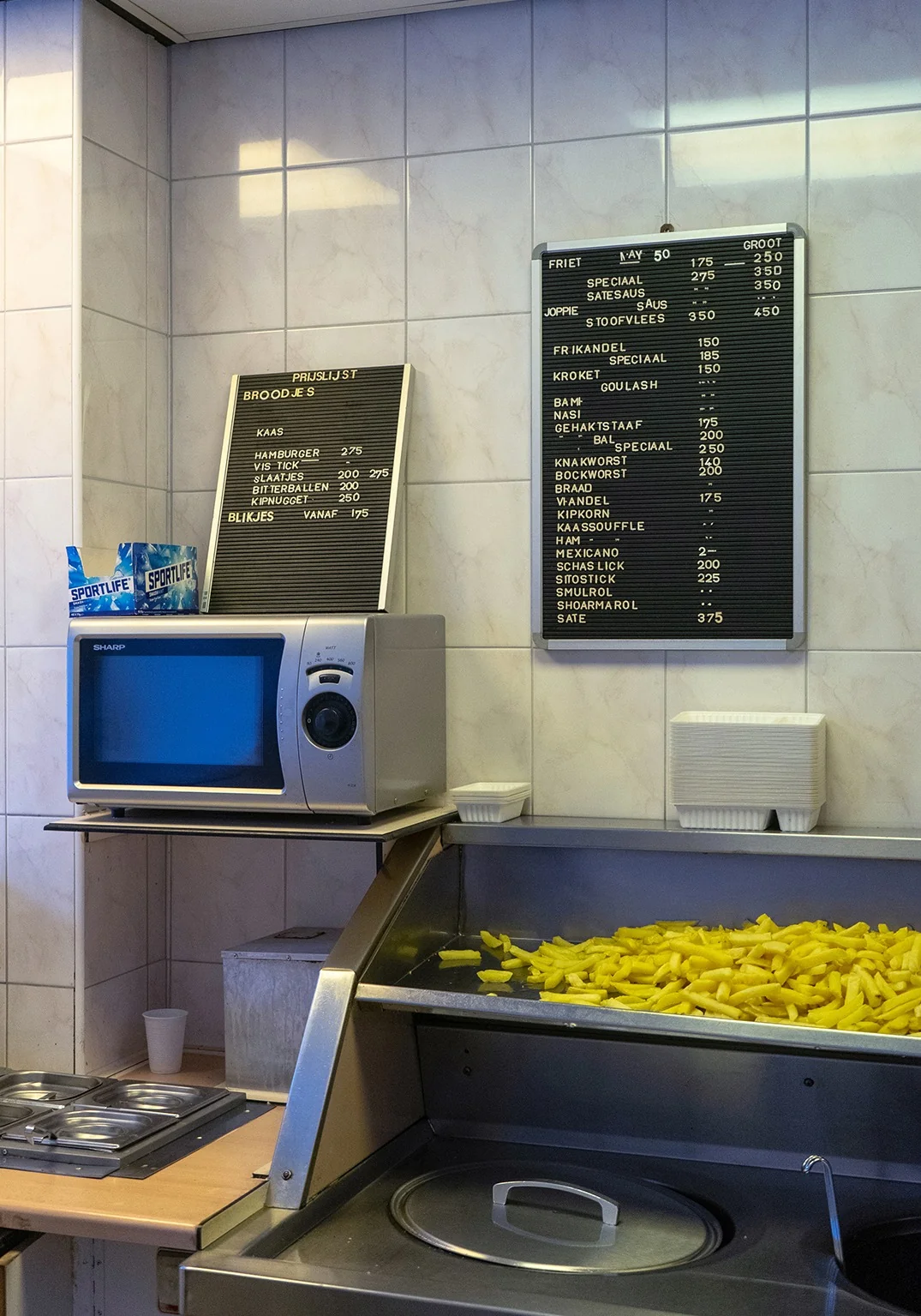 Interieur van een snackbar met prijslijsten, frituurbak en verse friet.