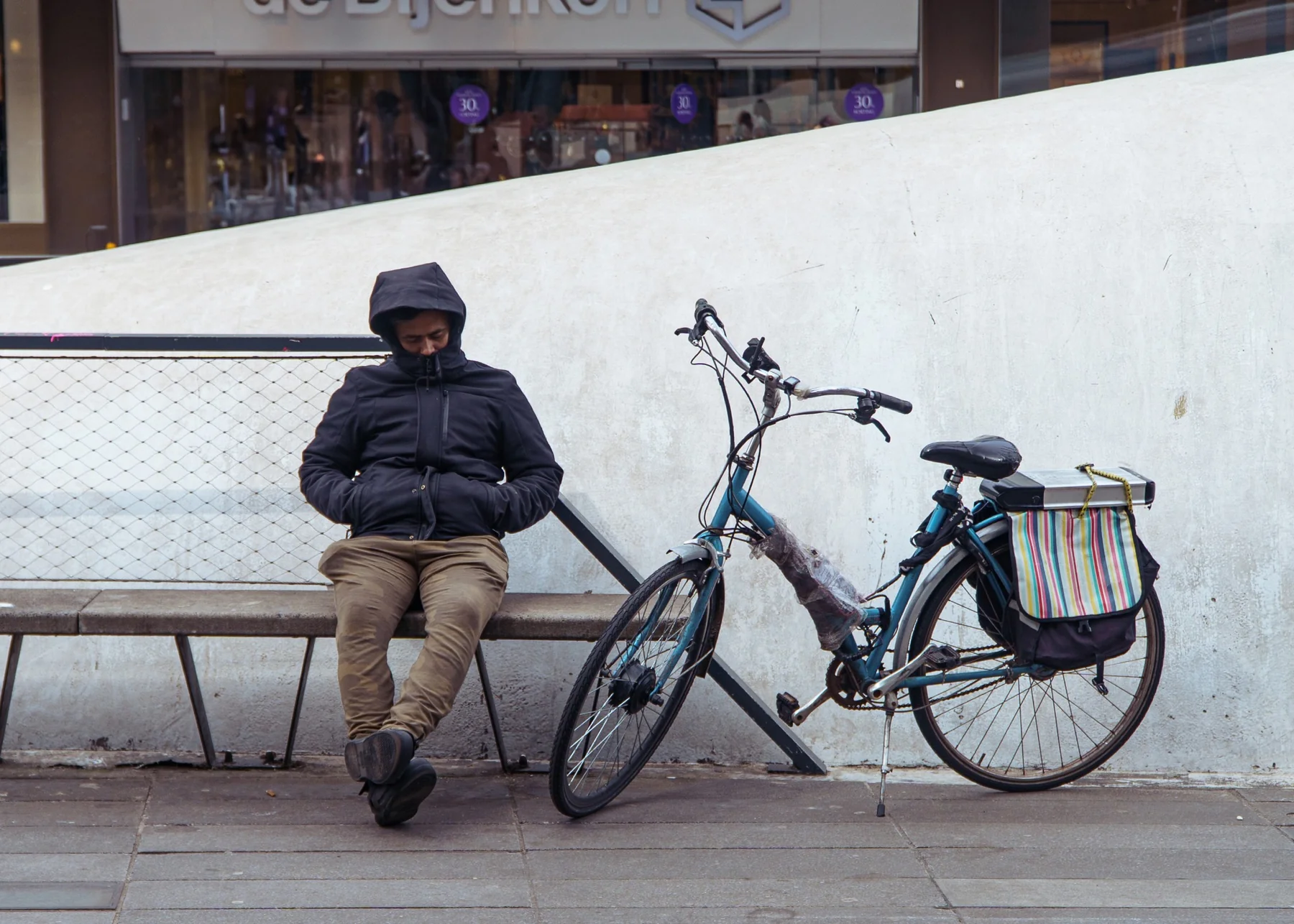 Een persoon rust op een bank naast een fiets in de openbare ruimte.