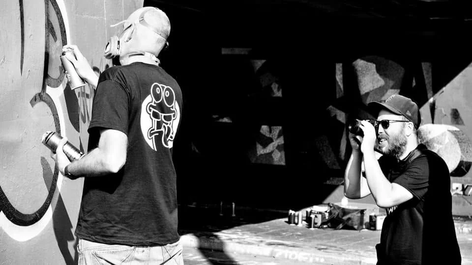 Fotograaf documenteert een street-artmaker tijdens het schilderen.